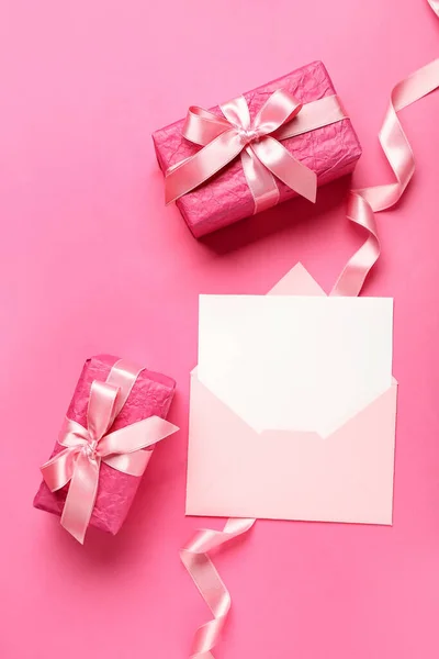 Envelope with blank card and gift boxes on pink background. Hello spring