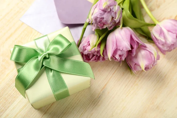 Gift box and beautiful tulip flowers on light wooden background. Hello spring