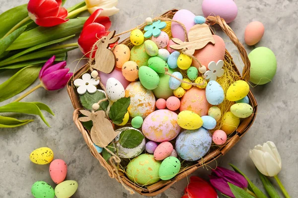Basket with painted Easter eggs, decor and tulip flowers on grunge background
