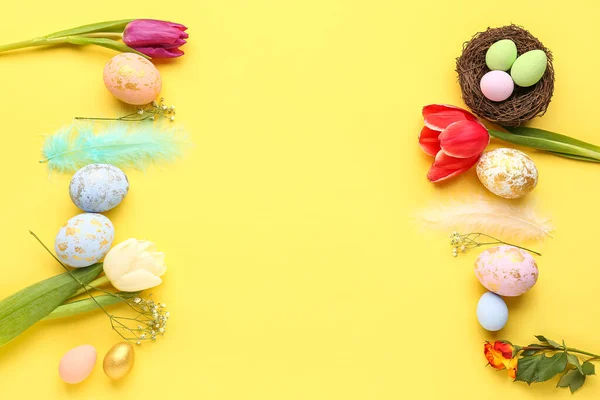 Composition with beautiful Easter eggs, feathers and flowers on yellow background