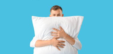 Young man hugging pillow on blue background