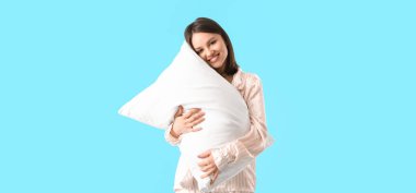 Beautiful young woman hugging pillow on blue background