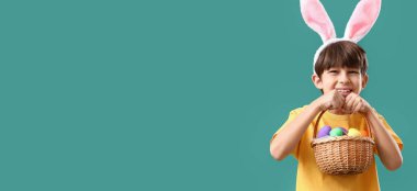 Little boy with basket of Easter eggs and bunny ears on green background with space for text