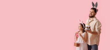 Little girl and her father with Easter eggs, cake and bunny ears on pink background with space for text