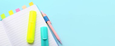 Notebook with markers and pen on light blue background with space for text