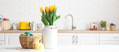 Paskalya yumurtaları, tavşan ve açık mutfakta yemek masasında bir buket lale.