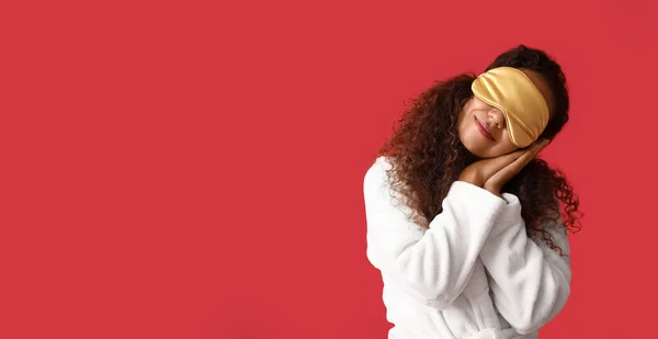 Young African-American woman in sleep mask on red background with space for text