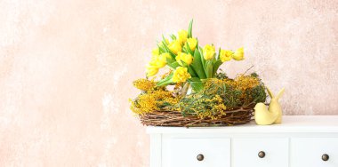 Wreath with beautiful spring flowers and Easter decor on table near grunge wall in room