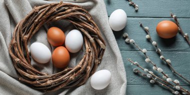 Easter composition with eggs, wreath and pussy willow branches on wooden background