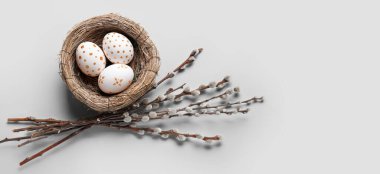 Nest with painted Easter eggs and pussy willow branches on light background