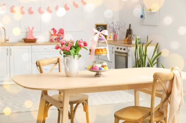 Easter cakes, eggs and tulips on dining table in kitchen