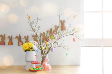 Stand with Easter eggs, beautiful flowers and stylish decor on table in room