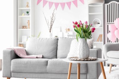 Vase with tulips on table in living room decorated for Easter celebration