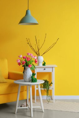 Vase with tulips and Easter rabbit on table in living room
