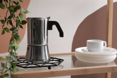 Shelving with geyser coffee maker, cups and plant on white and brown background