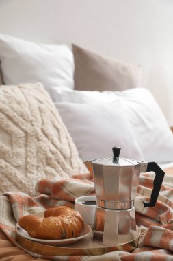 Plate with geyser coffee maker, delicious croissant and cup of espresso on bed