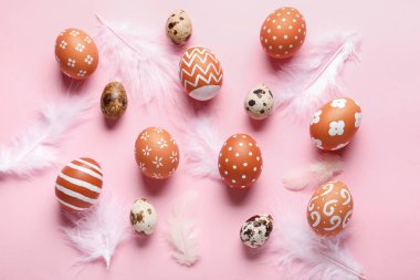 Composition with beautiful Easter eggs and feathers on pink background