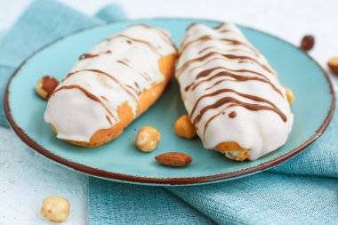 Plate with sweet eclairs, nuts and napkin on white background