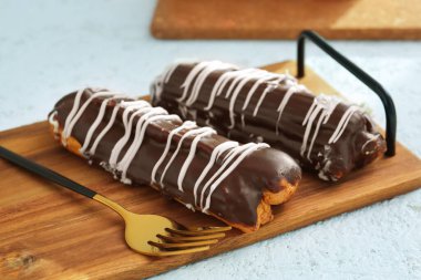 Board with delicious chocolate eclairs on white table