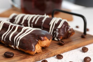 Board with delicious chocolate eclairs and coffee beans on white table