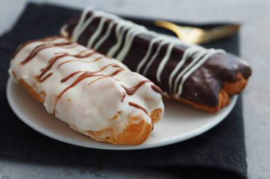 Plate with delicious eclairs on grey table