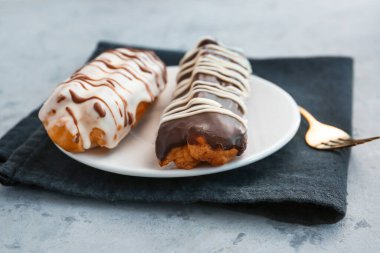 Plate with delicious eclairs on grey table