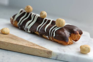 Board with delicious chocolate eclair and hazelnuts on grey table