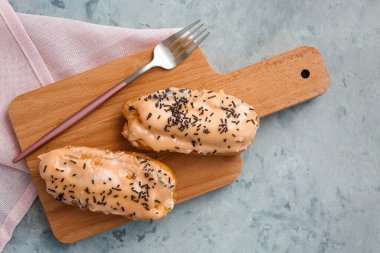 Board with delicious eclairs and fork on grey table