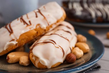 Plate with delicious eclairs and nuts on grey wooden table
