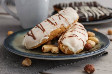 Plate with delicious eclairs and nuts on grey wooden table