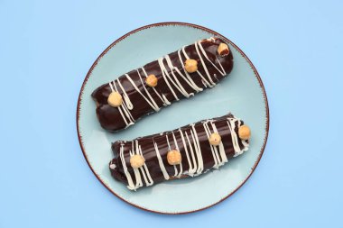 Plate with delicious chocolate eclairs on blue background