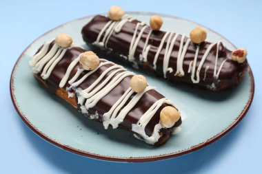 Plate with delicious chocolate eclairs on blue background