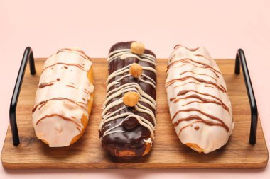 Board with delicious eclairs on pink background