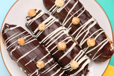 Plate with delicious chocolate eclairs on colorful background