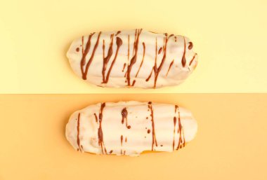 Tasty glazed eclairs on yellow and orange background