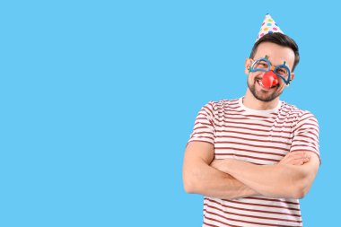 Funny young man in disguise on blue background. April Fools' Day celebration