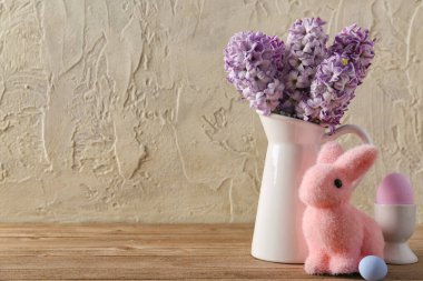 Vase with beautiful hyacinth flowers, painted eggs and Easter bunny on wooden table near grunge wall