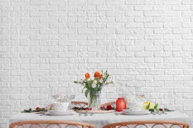 Table setting for International Women's Day celebration and vase with flowers in dining room near white brick wall