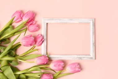 Beautiful tulip flowers and blank wooden frame on pink background