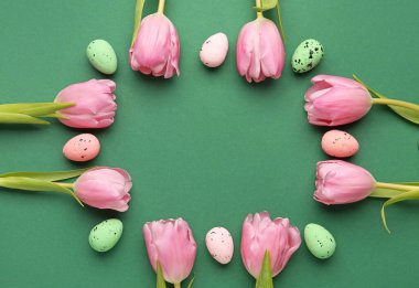 Frame made of beautiful tulip flowers and Easter eggs on green background