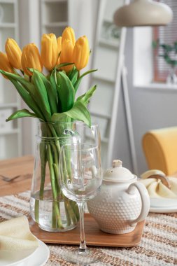 Table setting for International Women's Day celebration with tulip flowers and teapot in interior of room