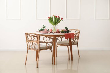 Table setting for International Women's Day celebration with tulip flowers, burning candles and eucalyptus branches in light room