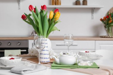 Table setting for International Women's Day celebration with tulip flowers and teapot in interior of room
