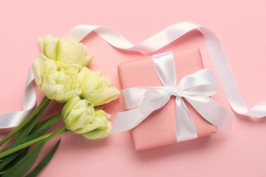 Gift box, ribbon and beautiful tulip flowers on pink background. Hello spring