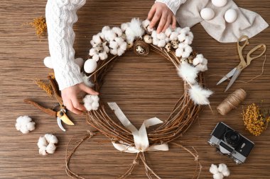 Woman making Easter wreath on wooden table, top view