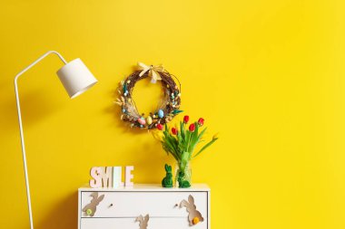 Interior of stylish room with Easter wreath, drawers and lamp