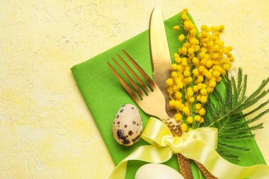 Table serving with Easter egg and mimosa flowers on yellow grunge background, closeup