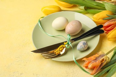 Table serving with Easter eggs and tulip flowers on yellow grunge background