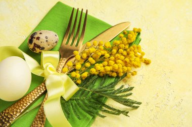 Table serving with Easter eggs and mimosa flowers on yellow grunge background, closeup