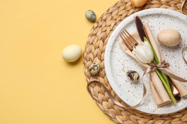 Table serving with Easter eggs and tulip flower on yellow background